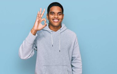 Gündelik kazak giyen genç, yakışıklı İspanyol adam gülümsüyor ve el ve parmaklarıyla 