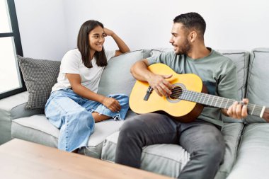 Genç latin çift evdeki kanepede oturup klasik gitar çalıyor..