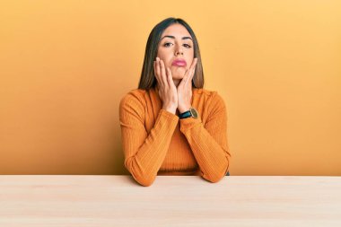 Gündelik giysiler giyen genç İspanyol kadın masada oturuyor. Yorgun eller, yüzünü kapatıyor. Depresyon ve üzüntü yaşıyor. 