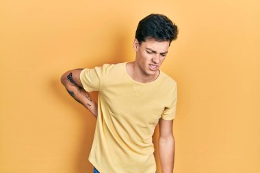 Sırt ağrısı çeken sıradan sarı tişörtlü genç İspanyol adam, elle dokunuyor, kas ağrısı çekiyor. 
