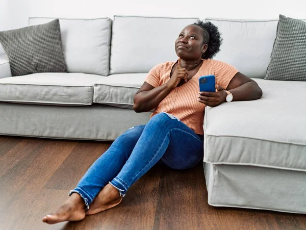 Mujer Africana Joven Usando Teléfono Inteligente Sentado Suelo Casa Pensando — Foto de Stock