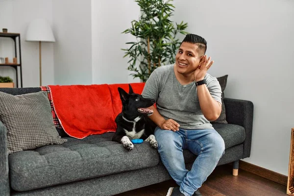 Jovem Latino Cachorro Sentado Sofá Casa Sorrindo Com Mão Sobre — Fotografia de Stock