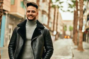 Genç Arap adam gülümsüyor, mutlu bir şekilde şehirde duruyor..