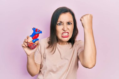 Orta yaşlı Latin bir kadın kalp orgu tutuyor öfkeyle bağırıyor, öfkeyle bağırıyor ve el kaldırıyor. 