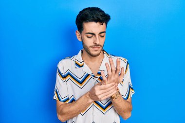 Günlük kıyafetler giyen genç İspanyol adam ellerinde ve parmaklarında ağrı, eklem iltihabı 