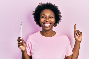 Elektrikli diş fırçası tutan Afrikalı Amerikalı genç bir kadın bir fikir ya da soruyla şaşırdı. 