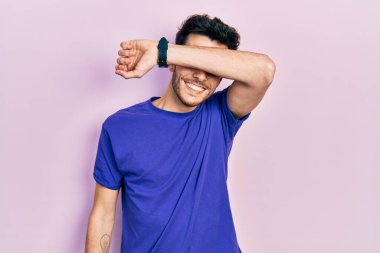 Gündelik tişört giyen, kollarıyla gözlerini kapatan neşeli ve komik gülümseyen genç İspanyol adam. kör kavram. 