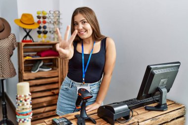 Perakende dükkanında açık mesajla pankart tutan genç esmer kadın üç numarayı gösterip işaret ederken kendinden emin ve mutlu bir şekilde gülümsüyor.. 