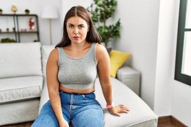 Evdeki kanepede oturan genç esmer kadın şüpheci ve gergin, sorun yüzünden surat asıyor. negatif kişi. 