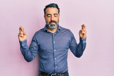 Orta yaşlı, sakallı, gri saçlı, iş kıyafetleri giyen, umut dolu ve gözleri kapalı bir şekilde el işareti yapan bir adam. Şans ve batıl inançlar. 