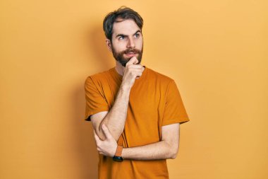 Sakallı, sıradan sarı tişörtlü beyaz bir adam bir soru hakkında endişeli ve gergin bir şekilde düşünüyor. 