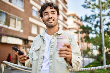 Güneşli bir günde akıllı telefon kullanarak mutlu bir şekilde gülümseyen sakallı yakışıklı İspanyol adam.