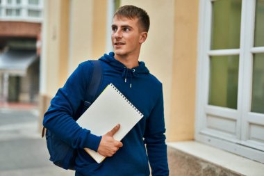 Üniversitede elinde defterle gülümseyen sarışın genç bir öğrenci..