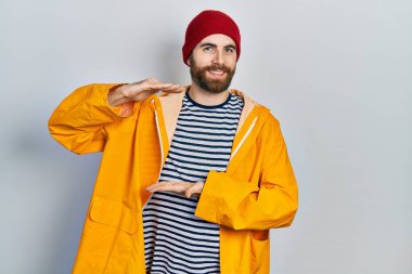 Sakallı, sarı yağmurluk giyen, elleri büyük ve büyük boy işareti gösteren beyaz bir adam. Ölçü sembolü. Kameraya bakıp gülümsüyor. ölçüm kavramı. 