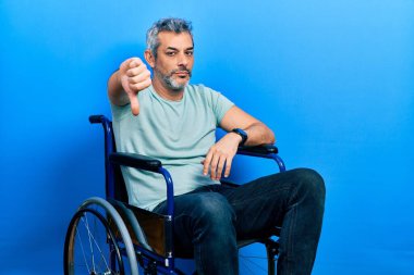 Tekerlekli sandalyede oturan yakışıklı, orta yaşlı bir adam. Mutsuz ve sinirli görünüyor. Reddedildiğini gösteriyor. kötü ifade. 