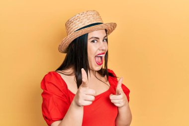 Yazlık şapkalı genç İspanyol kadın mutlu ve komik yüzüyle kamerayı işaret ediyor. iyi enerji ve titreşimler. 