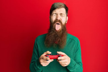 Kızıl saçlı, uzun sakallı, video oyunu oynayan, kumandalı, dilini dışarı çıkaran, komik bir ifadeyle mutlu bir adam.. 