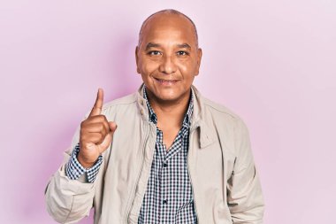 Orta yaşlı, gündelik kıyafetler giyen, bir fikir veya soruyla gülümseyen, mutlu bir yüzle işaret eden Latin bir adam. 