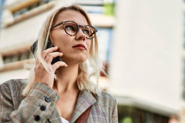 Şehirdeki akıllı telefondan konuşan ciddi yüzlü genç sarışın iş kadını..