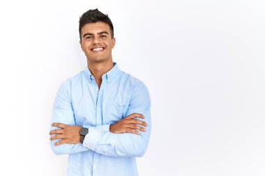 İzole edilmiş arka planda duran İspanyol gömlekli genç adam kameraya bakarken kollarını kavuşturup gülümsüyor. pozitif kişi. 