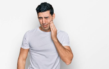 Yakışıklı, beyaz tişört giyen, diş ağrısı ya da diş hastalığından dolayı ağıza dokunan, acı dolu bir ifadeyle dokunan yakışıklı bir İspanyol. dişçi 