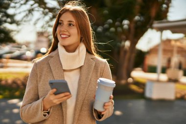 Genç kızıl saçlı kız akıllı telefon kullanıyor. Şehirde kahve içiyor..