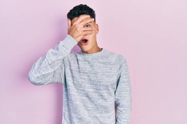 Gündelik kıyafetler giyen genç İspanyol adam şok içinde yüzünü ve gözlerini kapayarak utanmış ifadesiyle parmaklarından bakıyor.. 