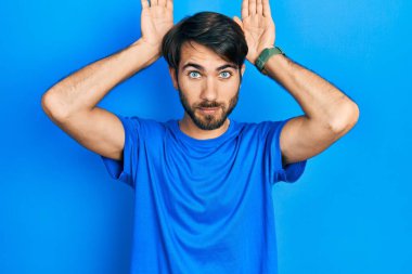 Gündelik kıyafetler giyen, tavşan kulağı yapan, avuçlarıyla alaycı ve şüpheci görünen genç İspanyol bir adam. Paskalya tavşanı konsepti. 