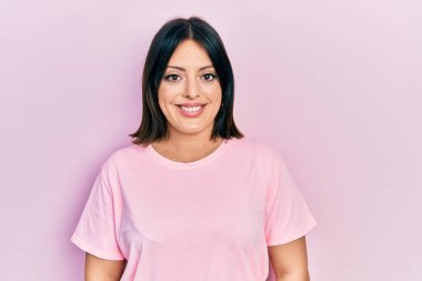 Yüzünde mutlu ve havalı bir gülümseme olan günlük pembe tişört giyen genç İspanyol kadın. şanslı kişi. 