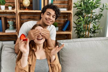 Mutlu gülümseyen genç çift ellerinde nişan yüzüğüyle kanepede oturuyor..