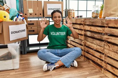 Bağış standında gönüllü tişört giyen Afro-Amerikalı genç bir kadın dokuz numarayı gösterip işaret ederken kendine güvenen ve mutlu bir şekilde gülümsüyor.. 