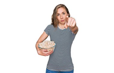 Patlamış mısır yiyen genç sarışın kadın kamerayı işaret ediyor ve sen kendinden emin bir şekilde ciddi görünüyorsun. 