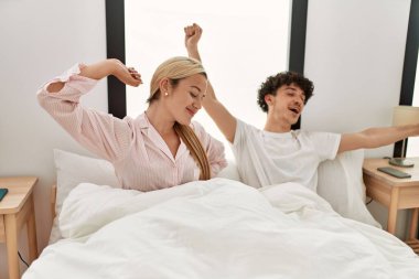Genç ve güzel bir çift kollarını esnetiyor ve yatakta oturuyorlar..