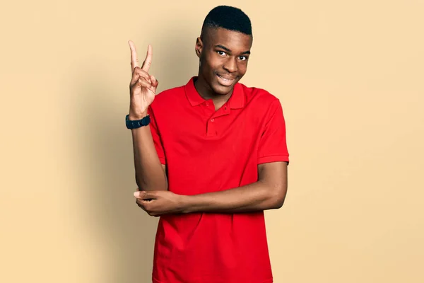 年轻的非洲裔美国人穿着休闲的红色T恤 喜形于色地微笑着 用手指在镜头前眨眼示意胜利 第二点 — 图库照片