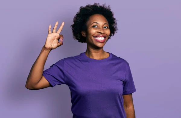 African american woman with afro hair wearing casual purple t shirt smiling positive doing ok sign with hand and fingers. successful expression.