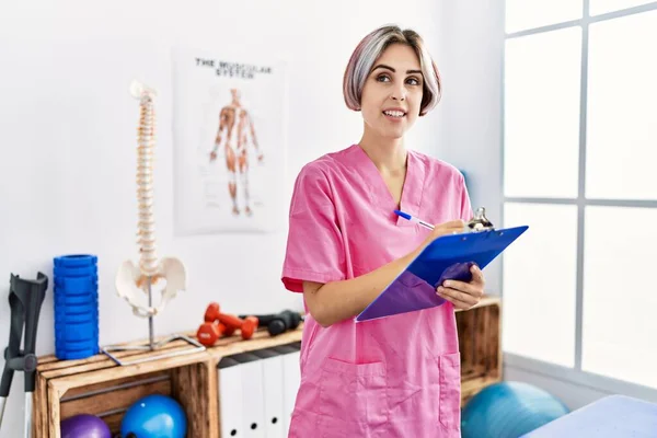 Joven Fisioterapeuta Caucásico Sonriendo Feliz Escritura Portapapeles Clínica —  Fotos de Stock