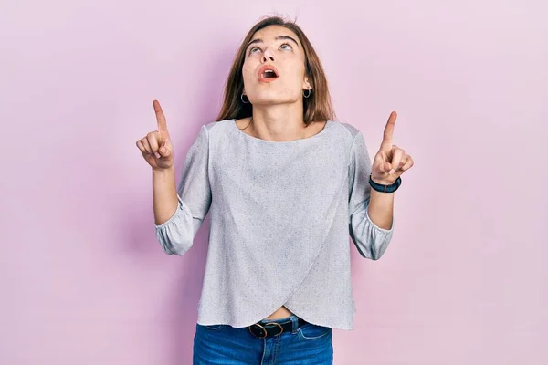 Mladá Běloška Neformálním Oblečení Užaslá Překvapená Dívá Nahoru Ukazuje Prsty — Stock fotografie
