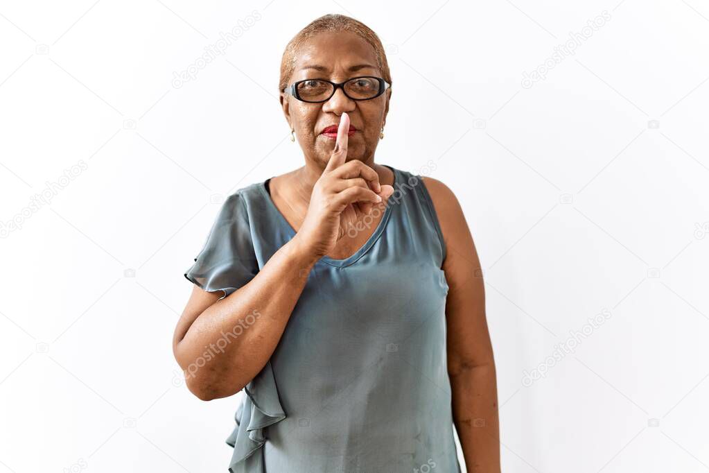 Mature hispanic woman wearing glasses standing over isolated background asking to be quiet with finger on lips. silence and secret concept. 