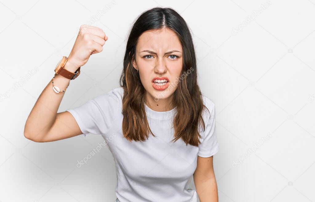 Young beautiful woman wearing casual white t shirt angry and mad raising fist frustrated and furious while shouting with anger. rage and aggressive concept. 