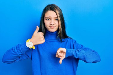 Balıkçı yaka kazak giyen genç esmer kız baş parmak hareketi yapıyor, anlaşmazlık ve anlaşma ifadesi. çılgın çatışma 