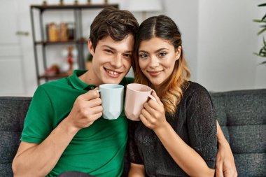 Genç beyaz çift gülümsüyor. Mutlu bir şekilde evde kahve içiyorlar..
