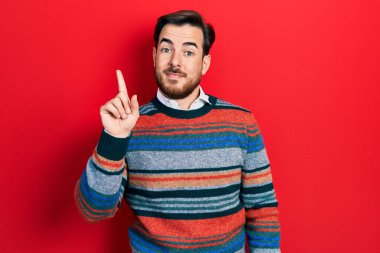 Sakallı, zarif yün kazak giyen yakışıklı beyaz adam bir numarayı gösterip işaret ederken kendinden emin ve mutlu gülümsüyor.. 