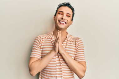 Makyaj yapan yakışıklı bir adam, sıradan bir tişört giyiyor, elleriyle dua ediyor, af diliyor, kendinden emin gülümsüyor.. 