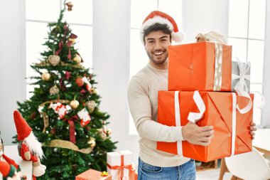 Genç İspanyol adam gülümseyerek mutlu bir şekilde evde hediyeler tutuyor..