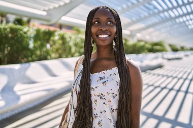 Genç Afrikalı Amerikalı kadın gülümseyerek şehirde mutlu mesut duruyor..