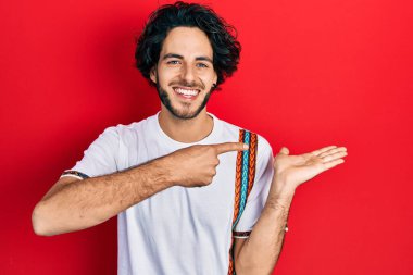 Beyaz tişört giyen yakışıklı İspanyol adam kameraya hayret ediyor ve gülümsüyor. Elle ve parmakla işaret ediyor.. 