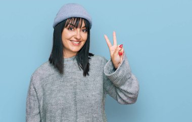 Şirin yün şapkalı genç İspanyol kadın kendini beğenmiş ve mutlu bir şekilde gülümserken iki numarayı işaret ediyor.. 