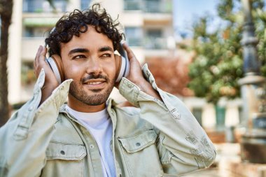 Yakışıklı, sakallı, neşeli, güneşli bir günde kulaklık takan bir İspanyol.