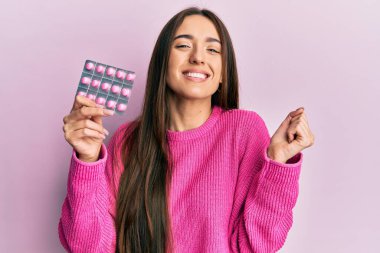 Genç İspanyol kız elinde haplarla gururla bağırıyor zaferi kutluyor ve başarıyı kollarını kaldırarak kutluyor. 