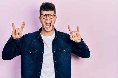 Günlük kıyafetler ve gözlük takan genç İspanyol adam çılgın bir ifadeyle bağırıyor elleri havada rock sembolü yapıyor. Müzik yıldızı. ağır kavram. 